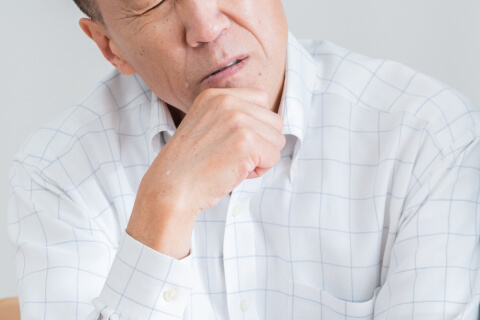 ことばが出づらく口元に手を当てて考え込む男性のイメージ